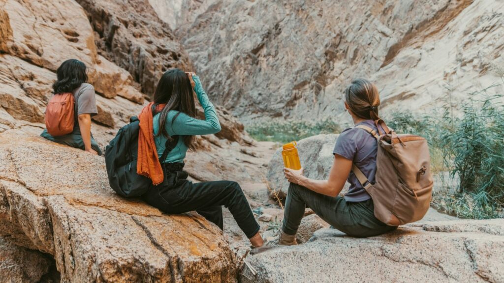 Drie vrouwen met rugzakken pauzeren tijdens een hike in een rotsachtig bergomgeving