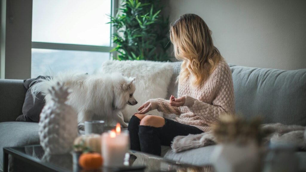 Vrouw op een rustige woningbank met hond, omringd door zachte materialen en sfeervolle kaarsen