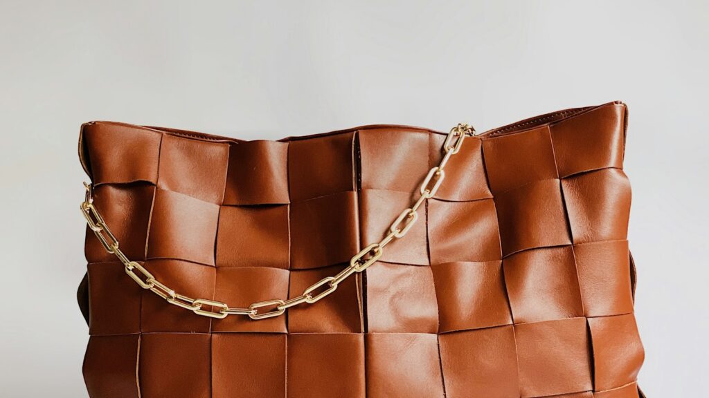 Bruine geweven leren tas met goudkleurige schakelketting, symbool voor de betekenis van je tas